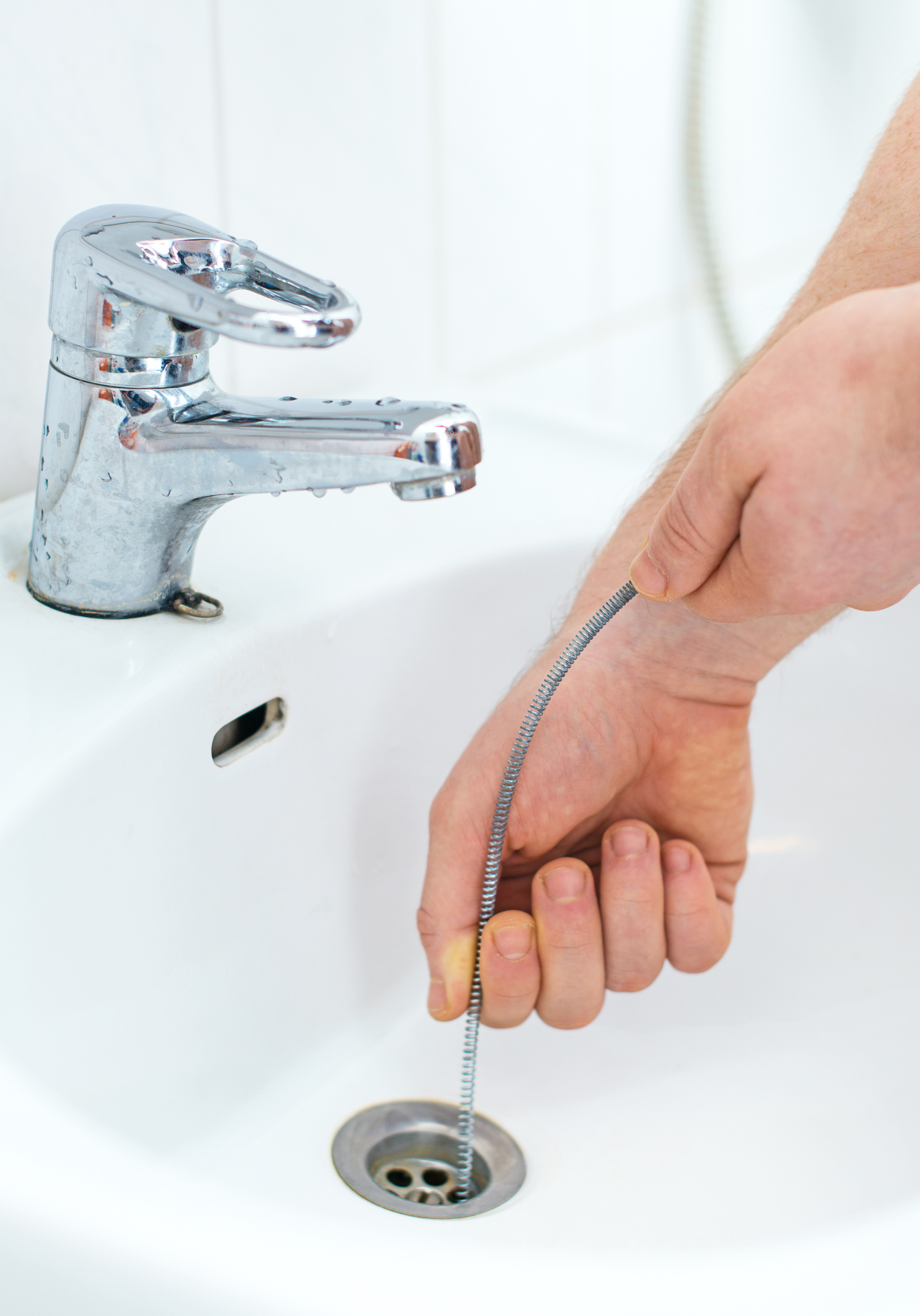 Close up image o someone using a bathroom snake to unclog a bathroom sink