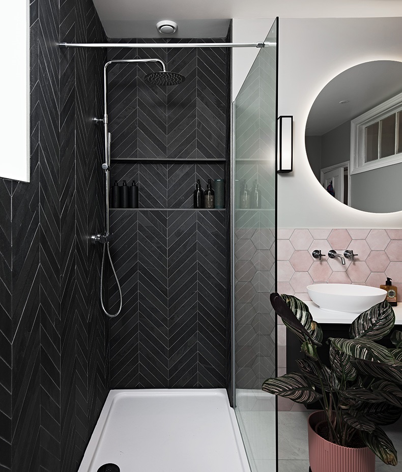 Close up lifestyle image of a shower enclosure with black tiles arranged in a chevron design