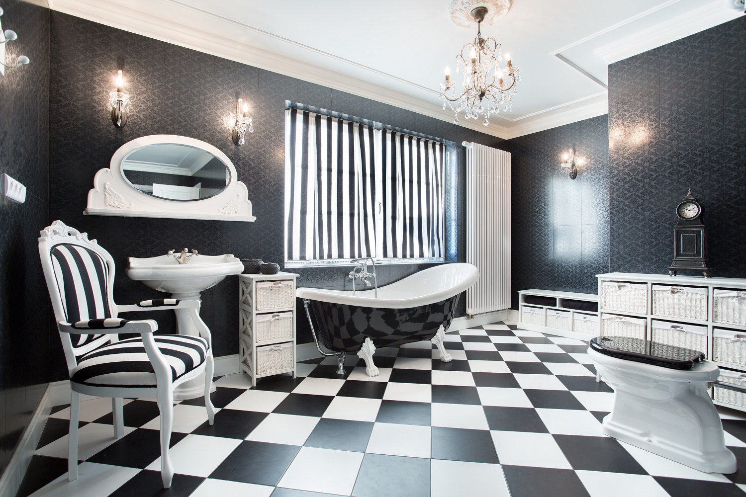 Lifestyle image of a black and white styled bathroom, with chequerboard floor tiles, striped chair, black patterned walls, a black slipper bath with painted white clawfeet and a white toilet with a black toilet seat, among other black and white bits and pieces