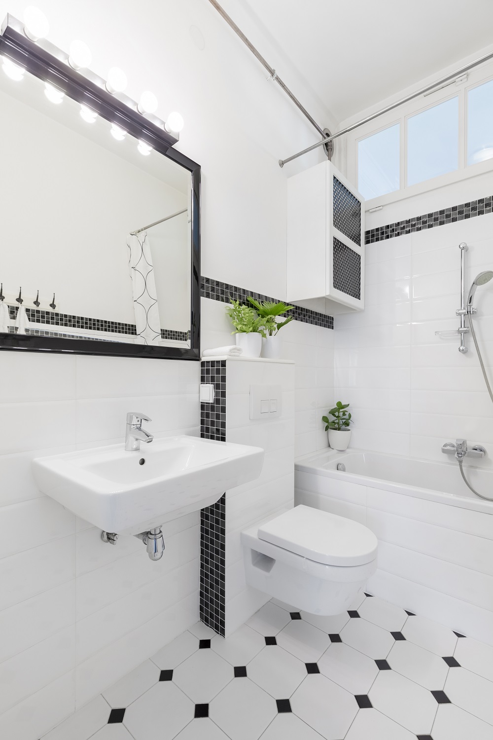 Lifestyle image of a small black and white bathroom, with black and white floortiles, black and grey mosaic detailing the white tile walls