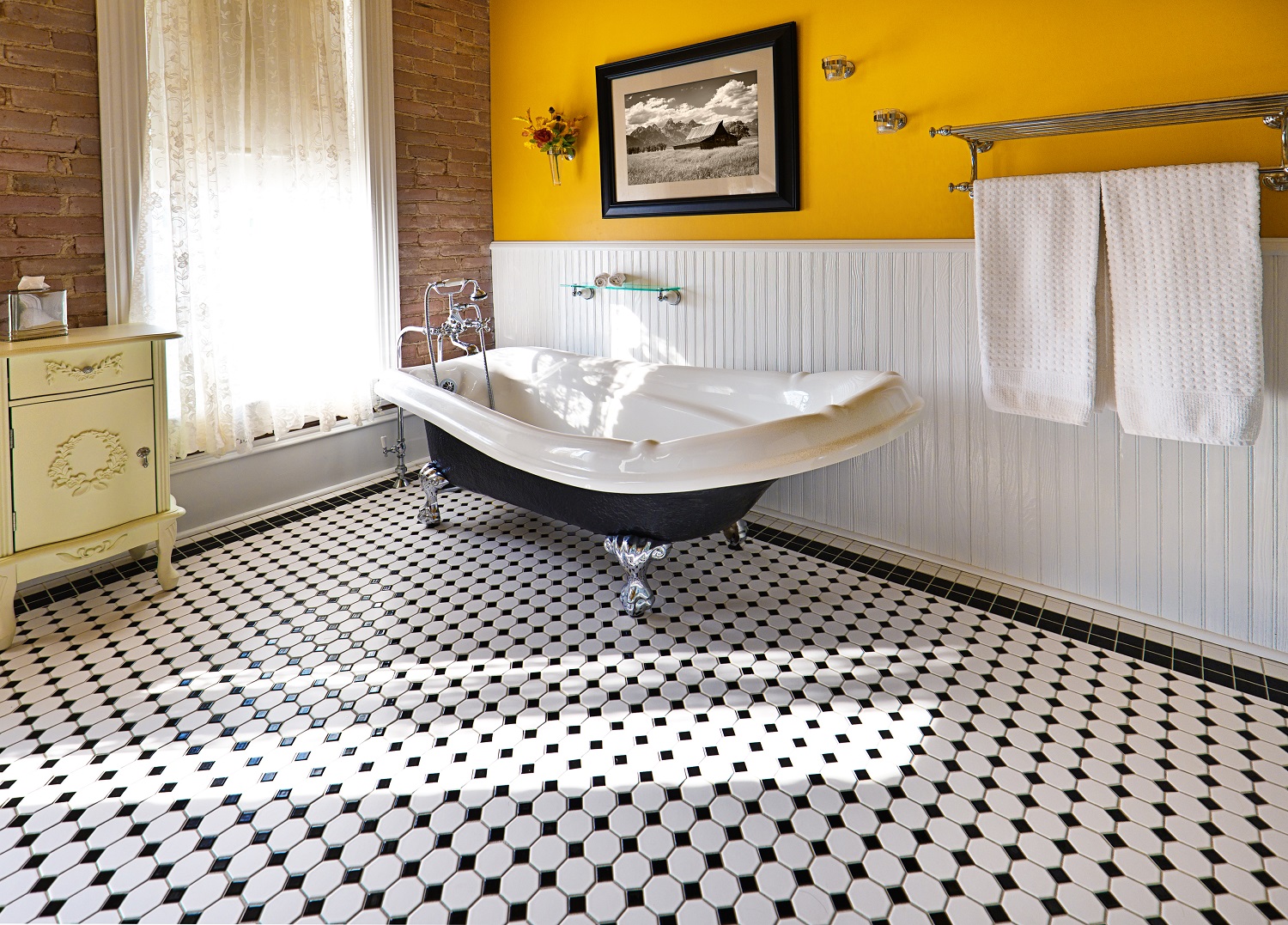 Lifestyle image of a black and white bathroom, with black and white floor tiles and a roll top bath with cast iron legs