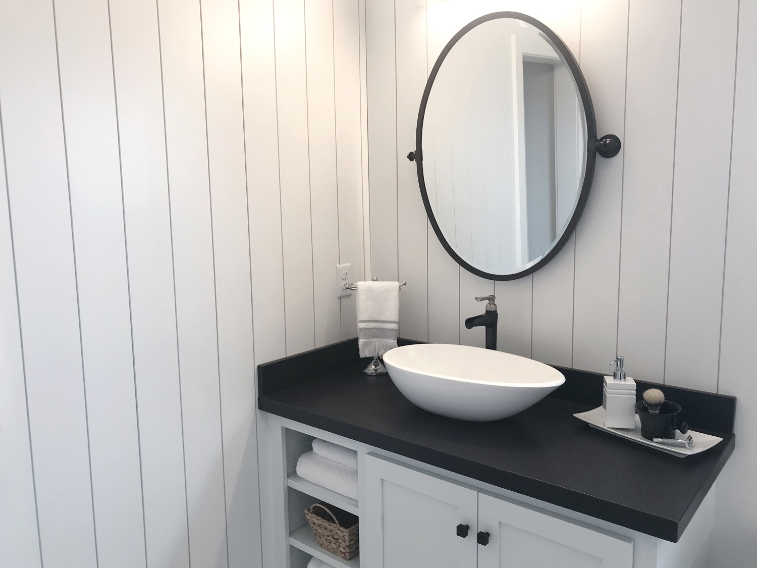 Close up lifestyle image of a black and white washbasin unit, with painted white wooden doors, black countertop, white countertop basin and matt black tall basin tap