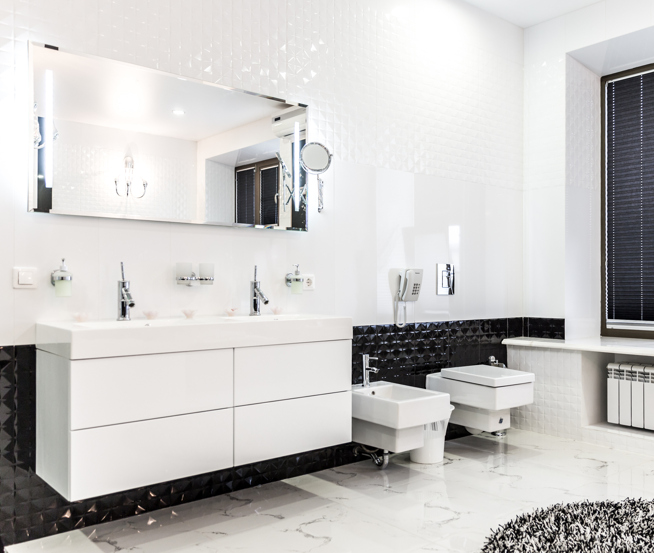 Lifestyle image of a black and white bathroom, with marble floor and a strip of black tiles along the lower part of the wall