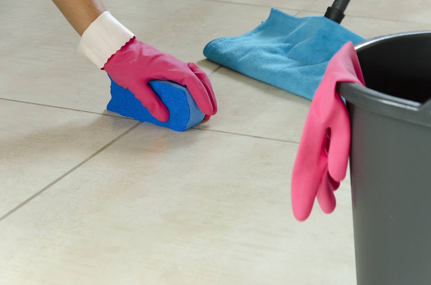 Close up product image of someone wearing pink rubber gloves cleaning their floor tiles with a sponge and mop