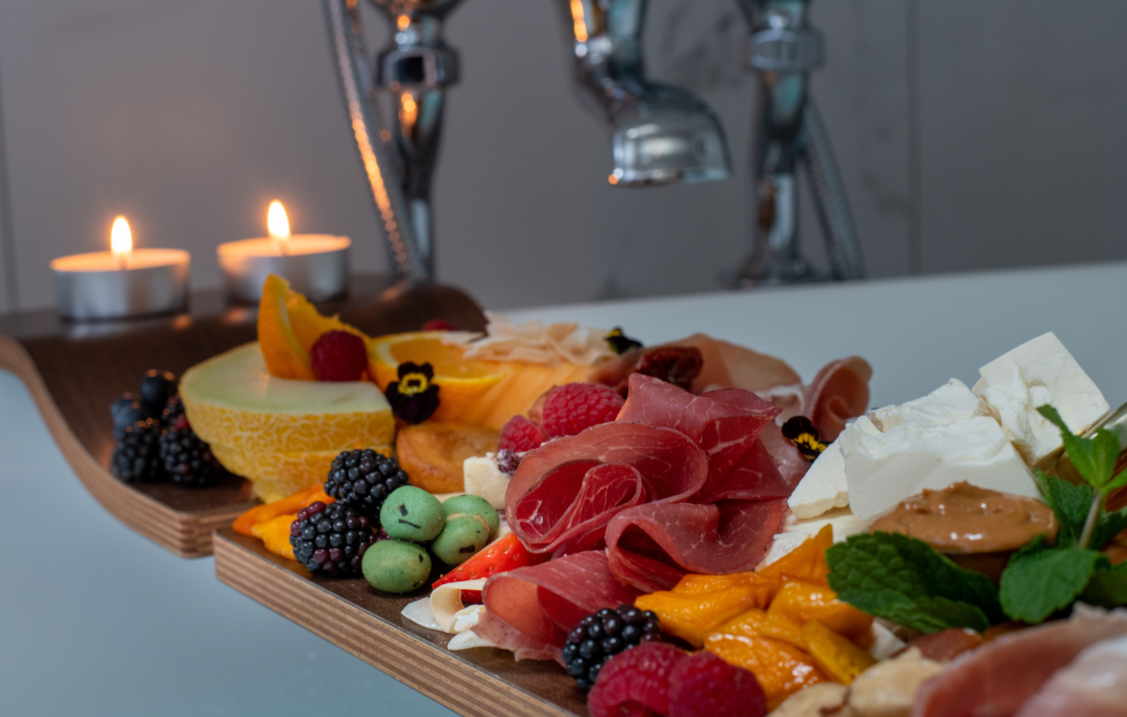 image of a bath board with charcuterie food items and two lit candles.