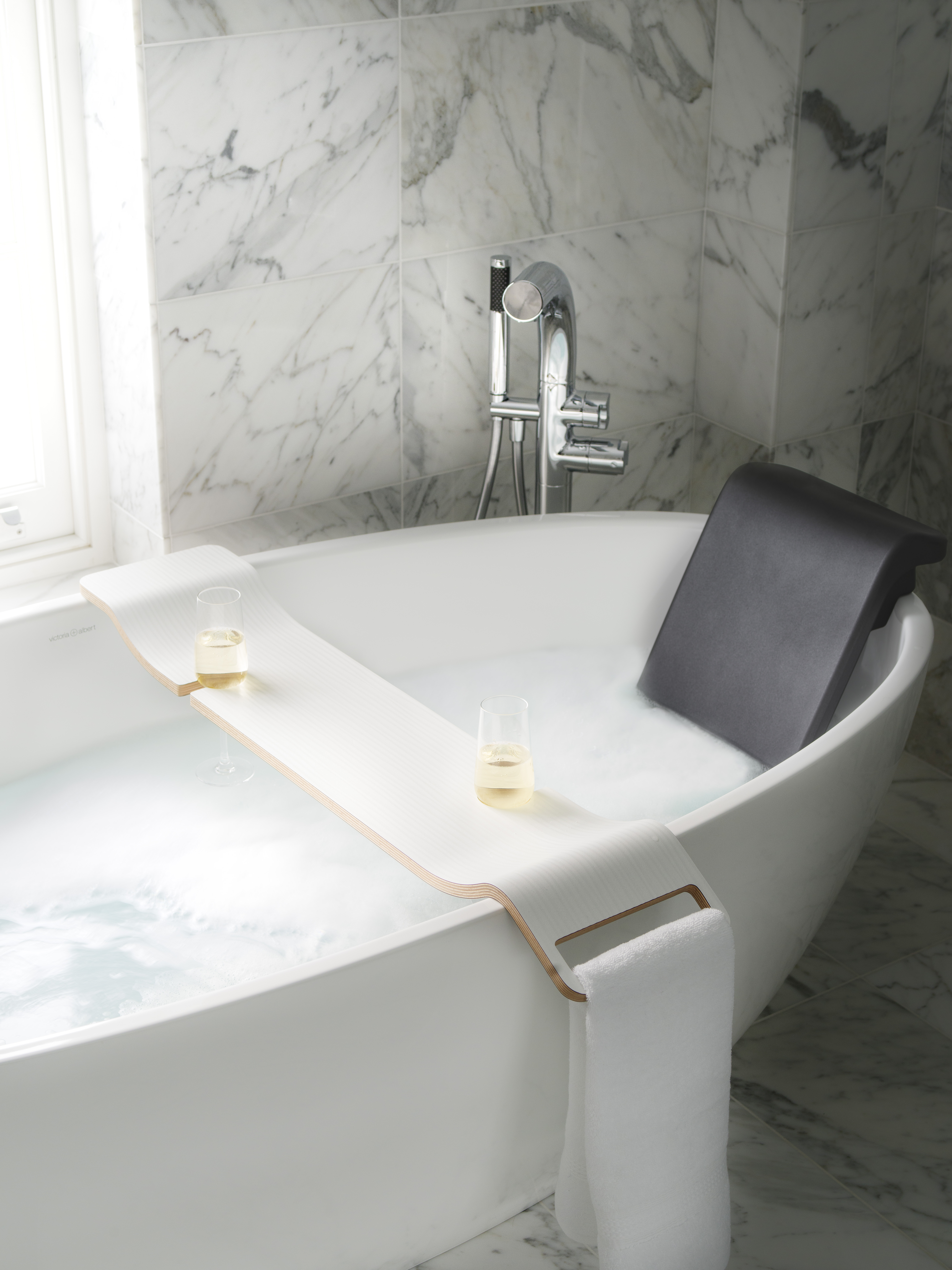image of filled freestanding bath with water, bath rack, glasses of wine and a towel hanging
