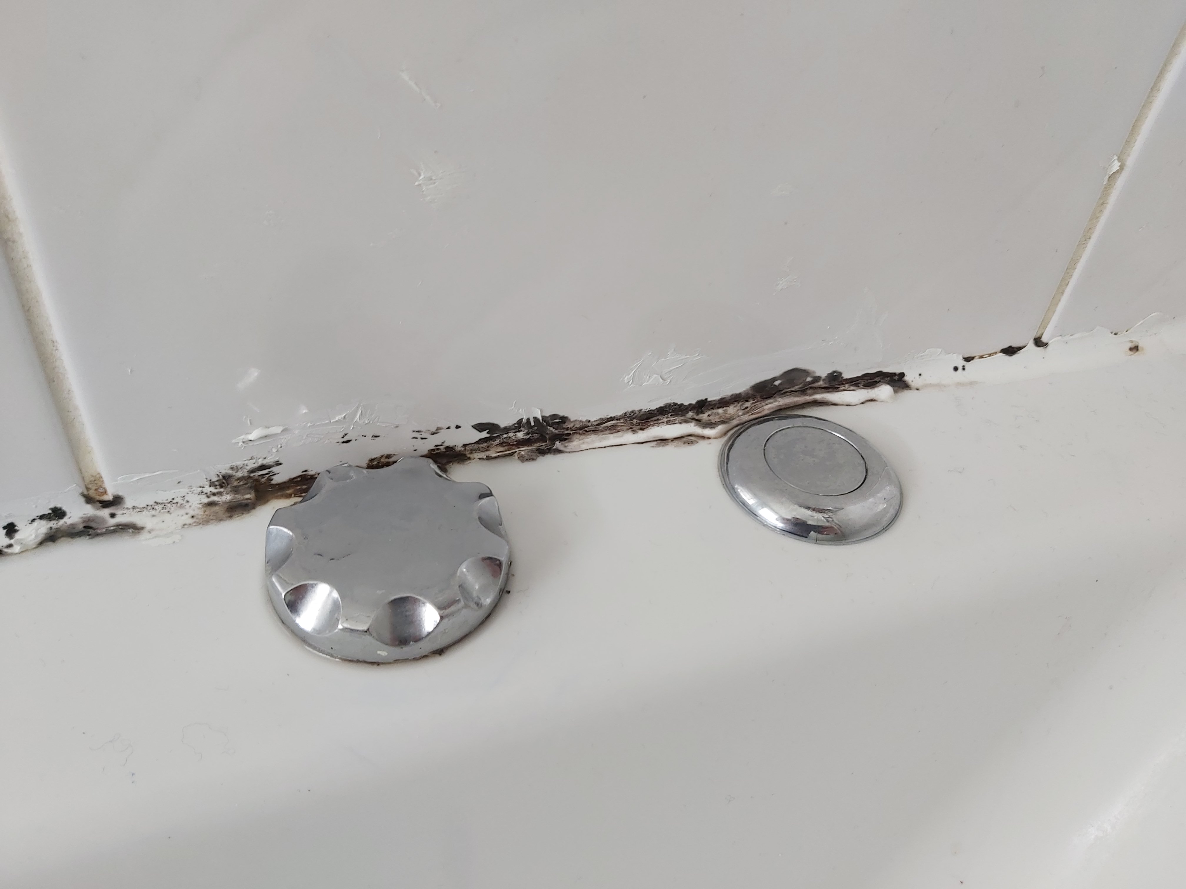 Close up image of limescale built up on the sealant around a bathtub