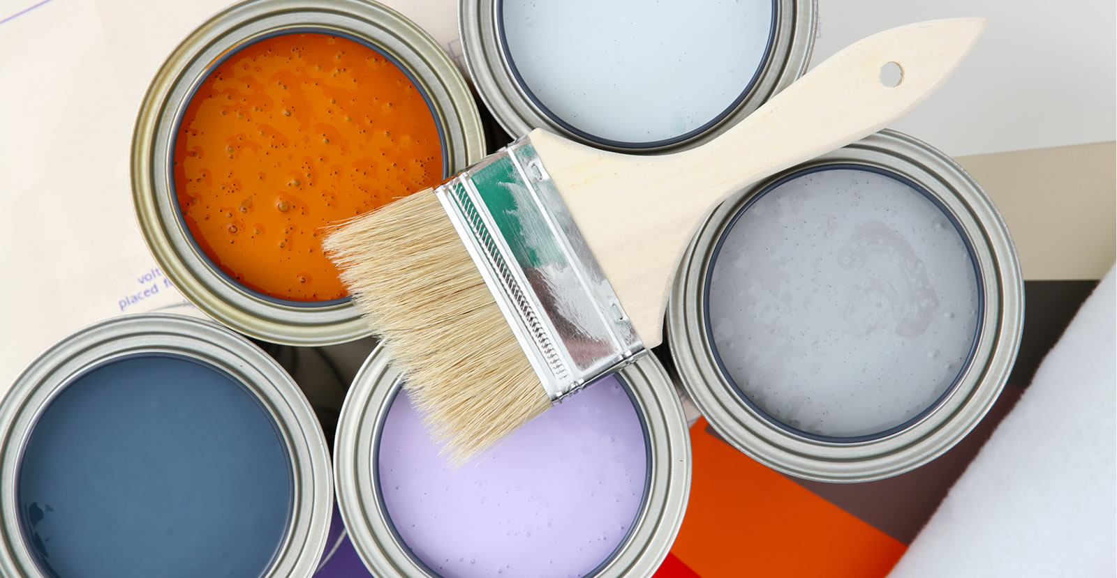 Close up image of a wide paintbrush resting on top of five paint cans