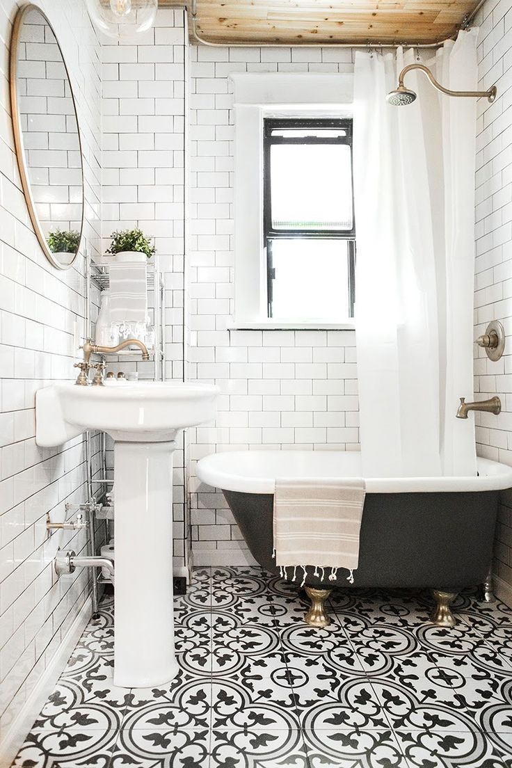 Lifestyle image of an Edwardian style bathroom, with black and white patterned floor tiles, white wall tiles and a wooden ceiling, a pedestal basin with brushed brass taps, an open chrome cabinet, a green roll top shower bath with brushed brass clawfeet, brushed brass bath filler and wall mounted shower head and a white shower curtain