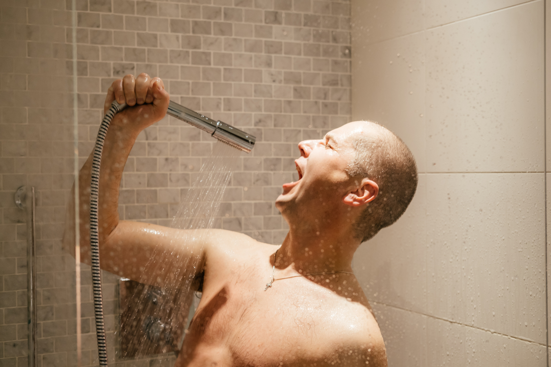 Lifestyle image of a bald man singing in the shower, holidng the handset shower like a microphone