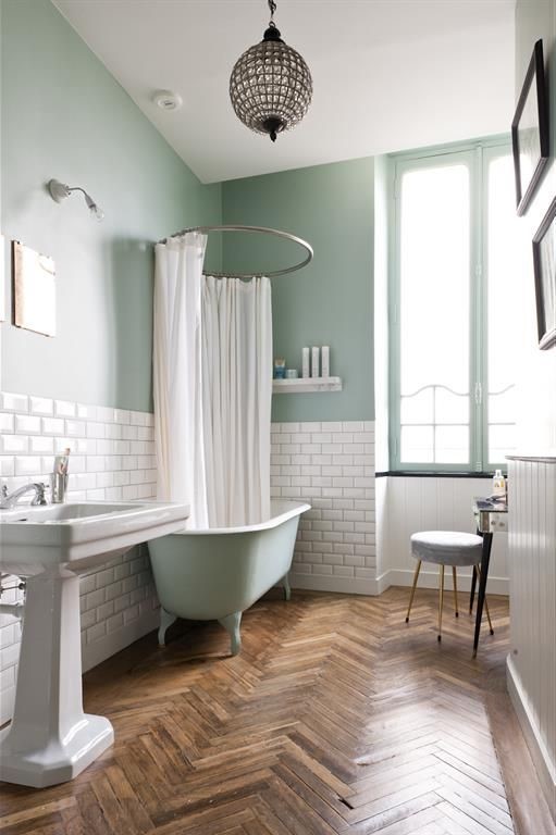 Lifestyle image of a green and white bathroom design, featuring pastel green painted walls, white wall tiles, pastel green painted roll top bath and a white pedestal basin