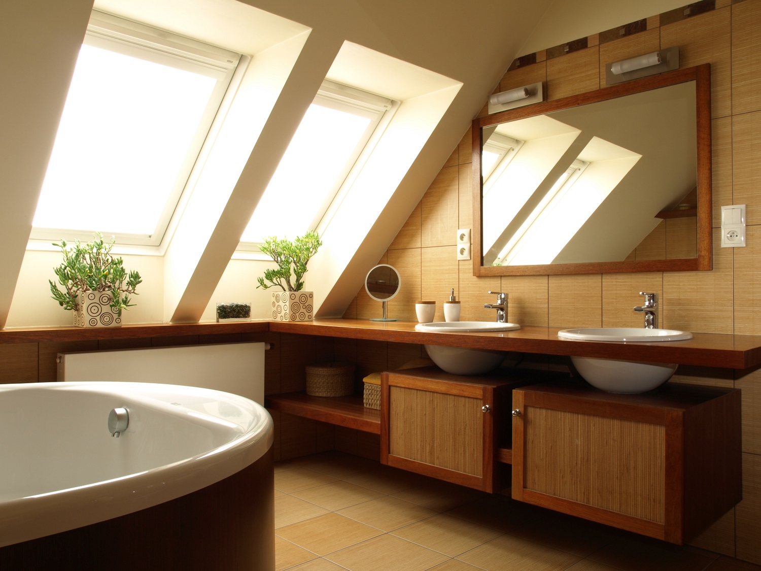 Lifestyle image of an attic bathroom, with tiled floor and walls, wooden wall mounted cabinets and countertop, freestanding bath and skylights