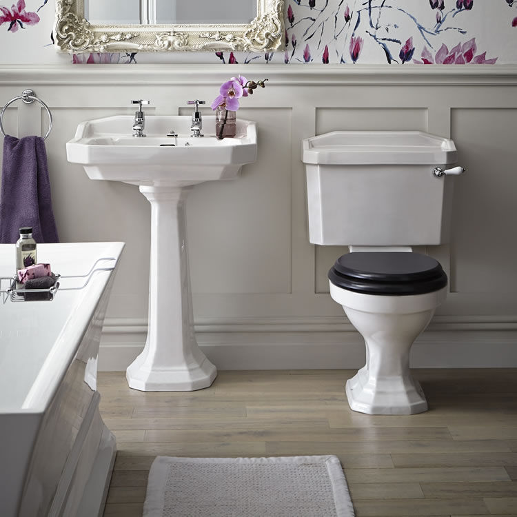 Lifestyle of a traditional style bathroom, with an open back close coupled toilet, a pedestal basin, a freestanding bath and wooden panelling on the walls