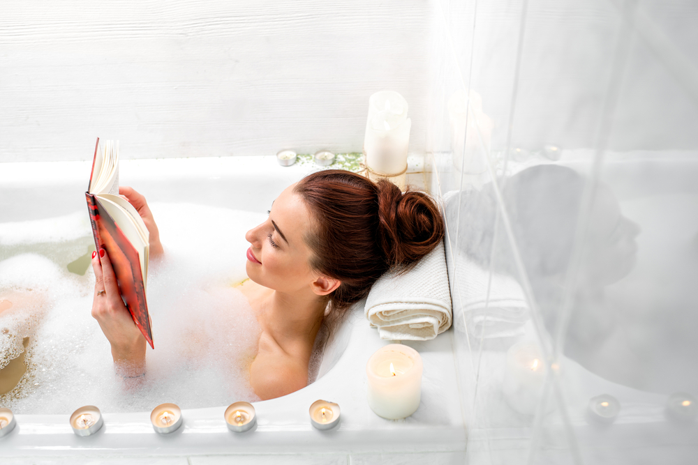 Lifestyle image of a woman reading a book in a bubble bath