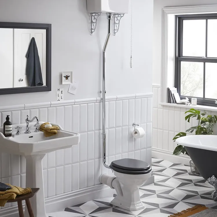 image of heritage granley high level toilet with black seat and chrome pipe and ornate cistern brackets in a grey and white star floor tiled bathroom window to right, fitted with pedestal basin and traditional freestanding bath and grey rectangle mirror.