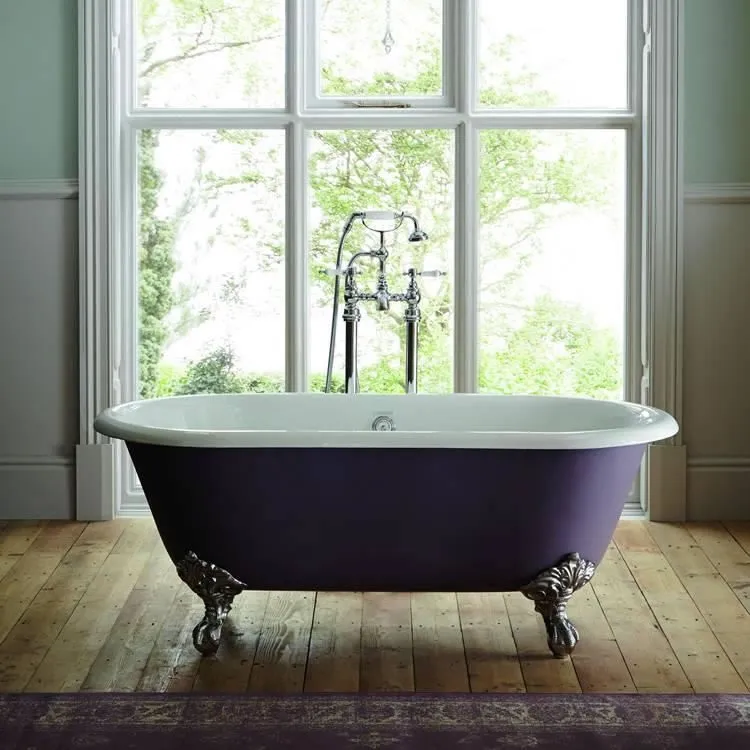 image of heritage baby buckingham double ended cast iron freestanding bath with period style legs and chrome freestanding bath shower mixer tap in front of a large window and on wooden slat flooring