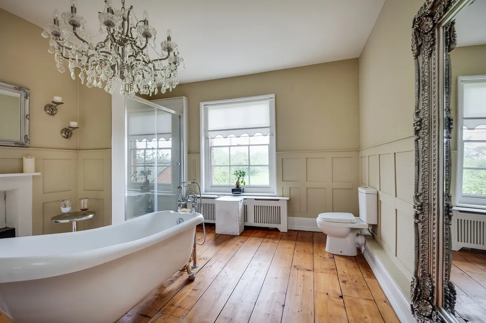 image of a wooden floor bathroom with roll top slipper bath close up and a shaker style wall with chandelier and big window