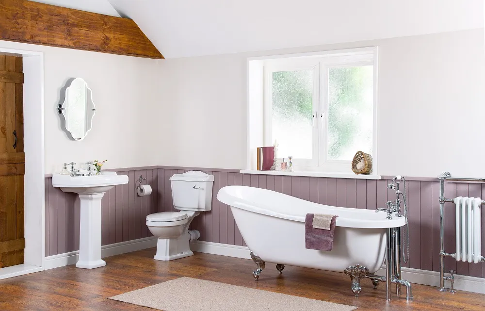 image of a traditional looking bathroom with a roll top slipper bath with chrome feet, a white and grey panelled wall, close coupled toilet, pedestal basin and mirror