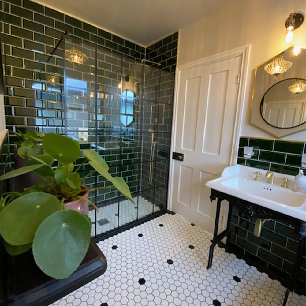 Lifestyle image of a Victorian styled bathroom, with black and white hexagonal floor tiles, dark green wall tiles, black washstand with a stepped washbasin and a crittall shower enclosure