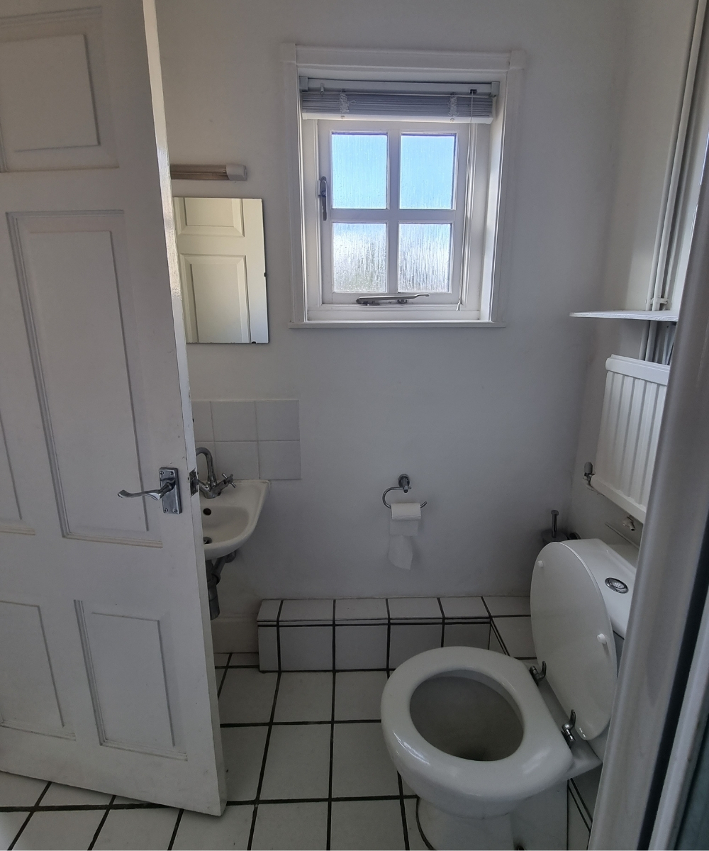 room shot of white tiled bathroom before renovation in guest cottage shower room looking from side towards window