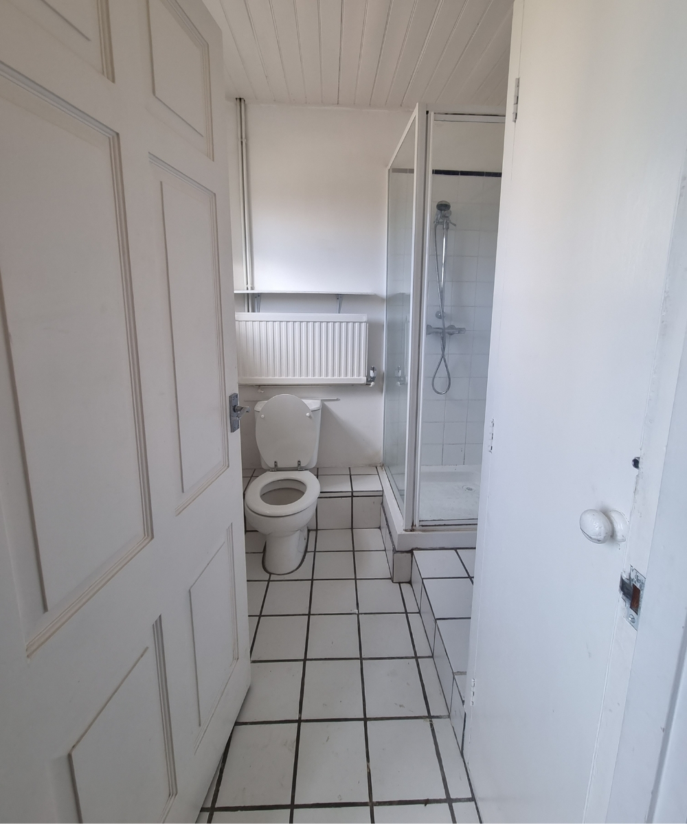 room shot of white tiled bathroom before renovation in guest cottage shower room looking from door