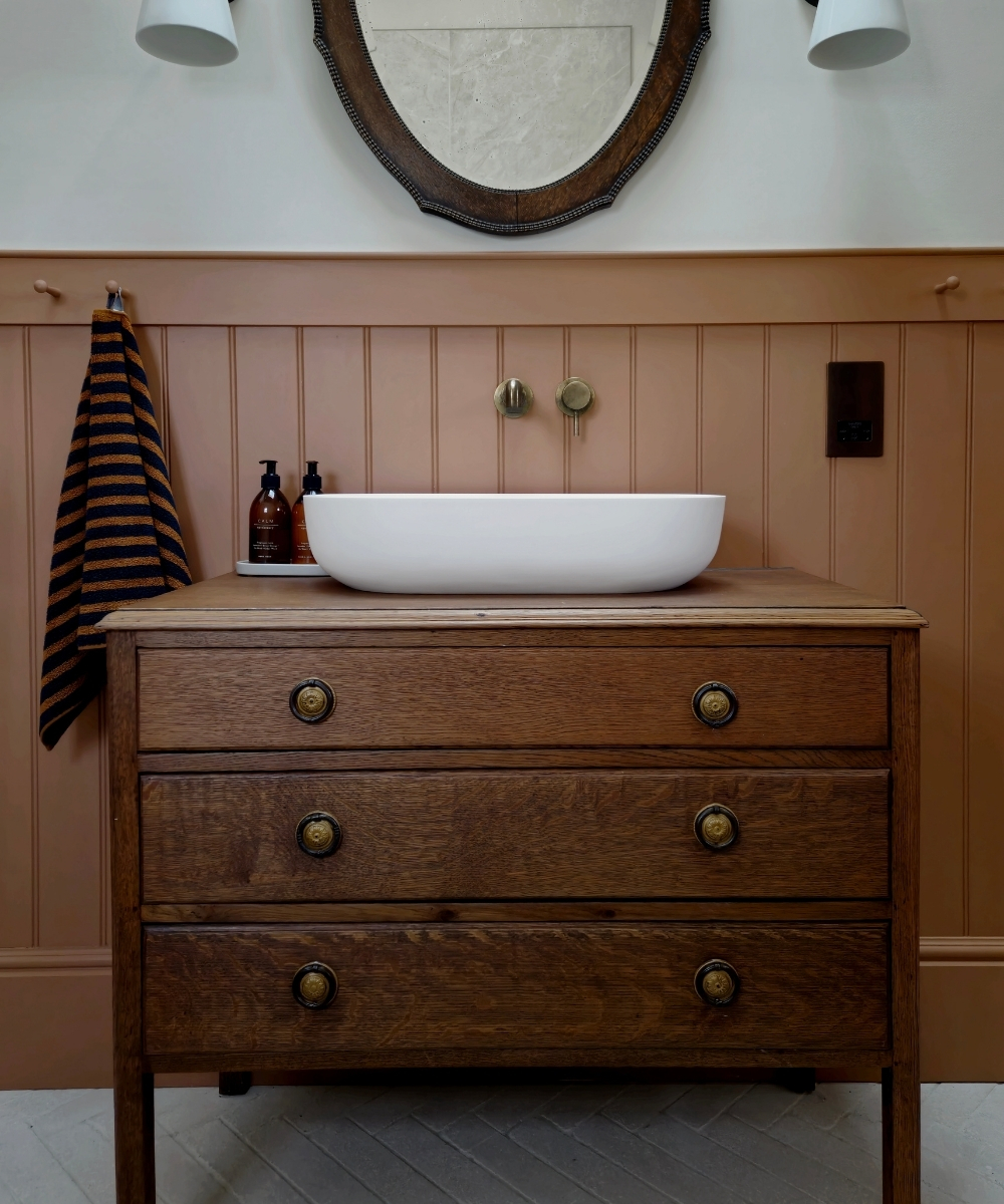 image of an old style vanity unit with knob handles fited with a countertop bowl above in brown wood panelled traditional period style bathroom
