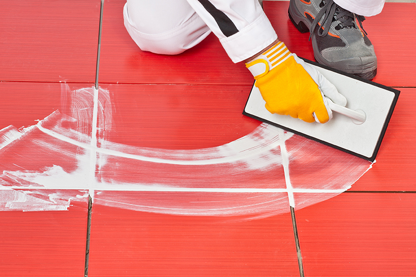 Close up image of someone sweeping the grout to ensure it is equally distributed between their floor tiles