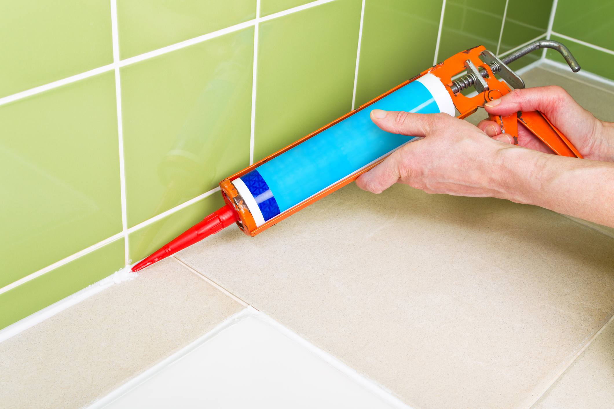 Close up image of a man using a sealant gun to replace the sealant around the edge of a bath