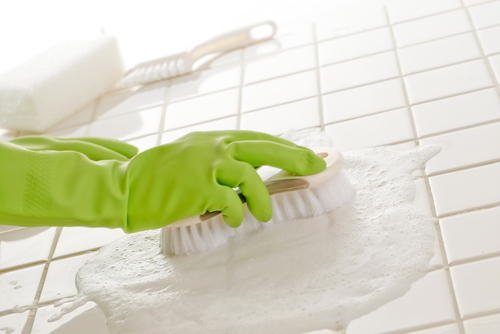 Close up image of someone cleaning bathroom tiles with a brush and soapy water
