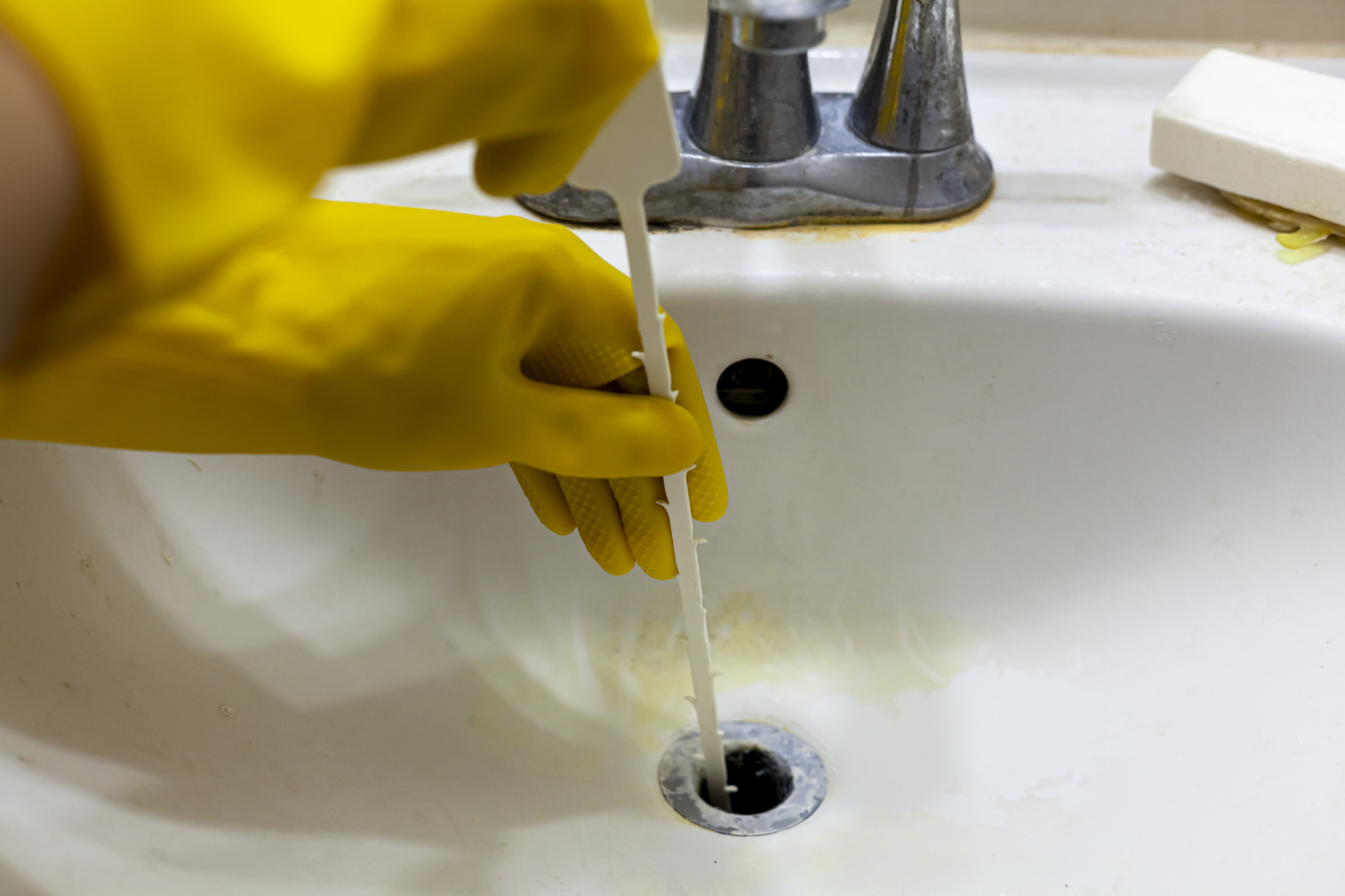 Close up image of someone using a snaker auger hair removal tool to unclog a bathroom sink