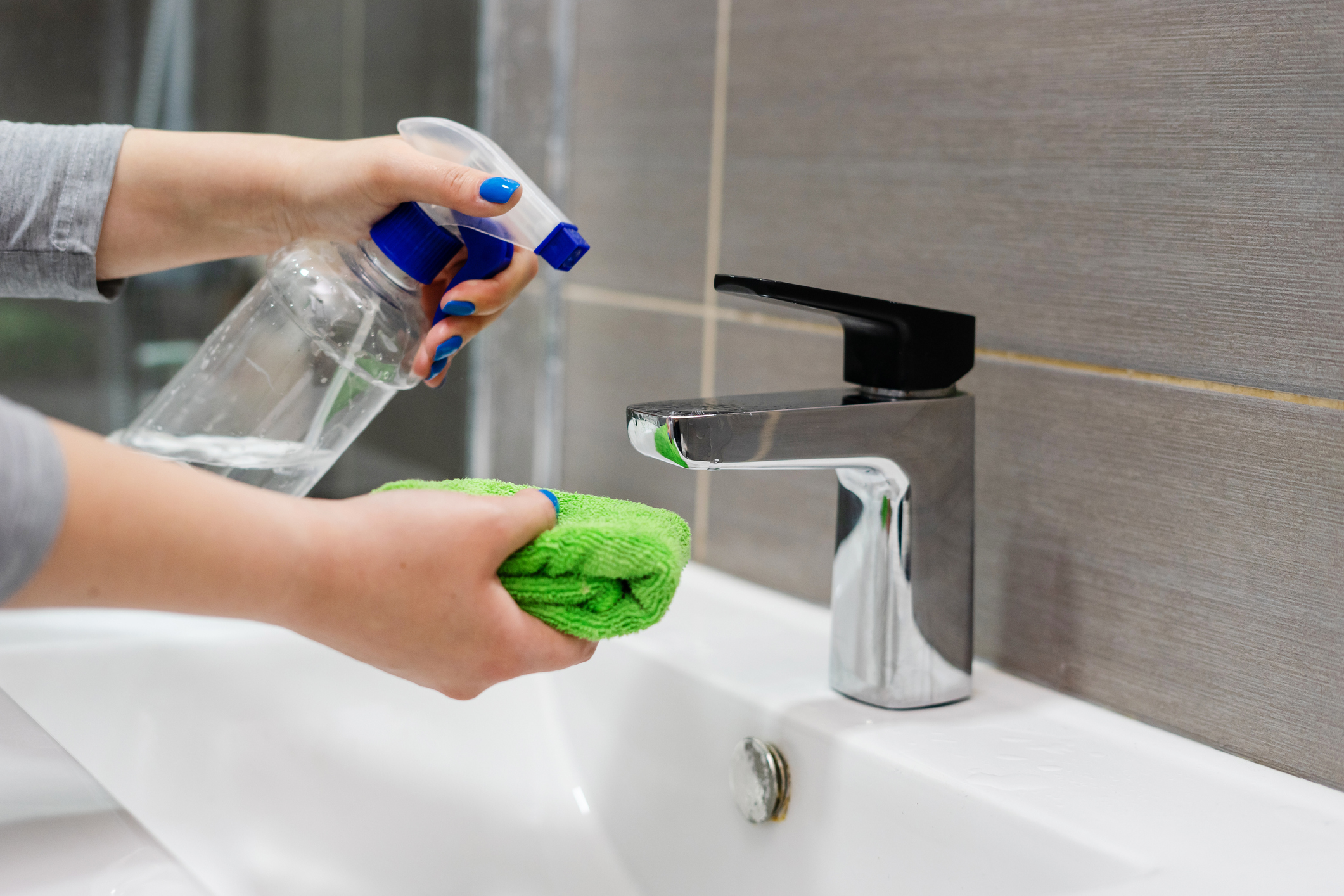 Close up image of a woman cleaning limescale off a tap using a spray bottle and damp cloth