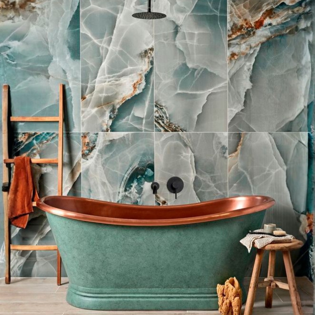 Lifestyle image of the BC Designs Verdigris Green Freestanding Boat Bath in front of blue-green marble wall panels