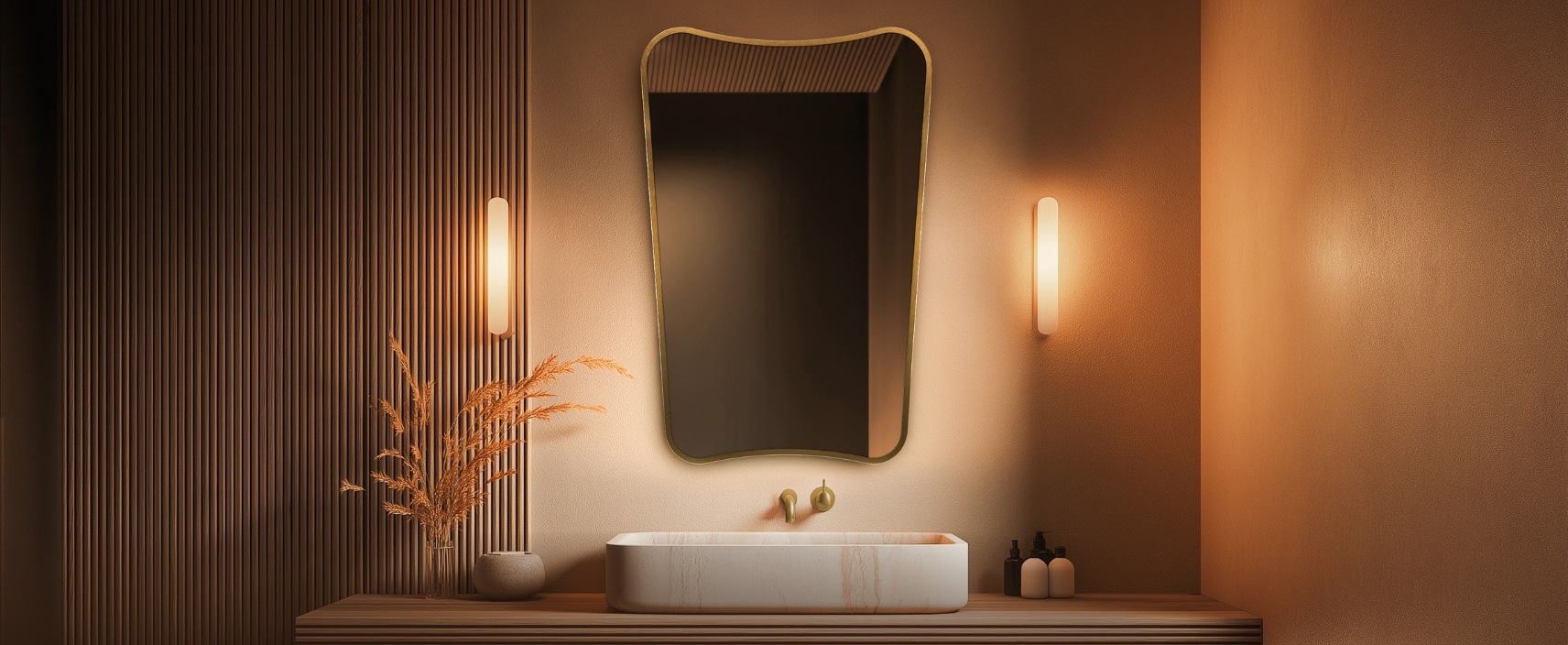 Lifestyle image of the Origins Living Delphine Curve 600mm x 900mm Brushed Brass Mirror above a marble-effect countertop basin and between wall lights