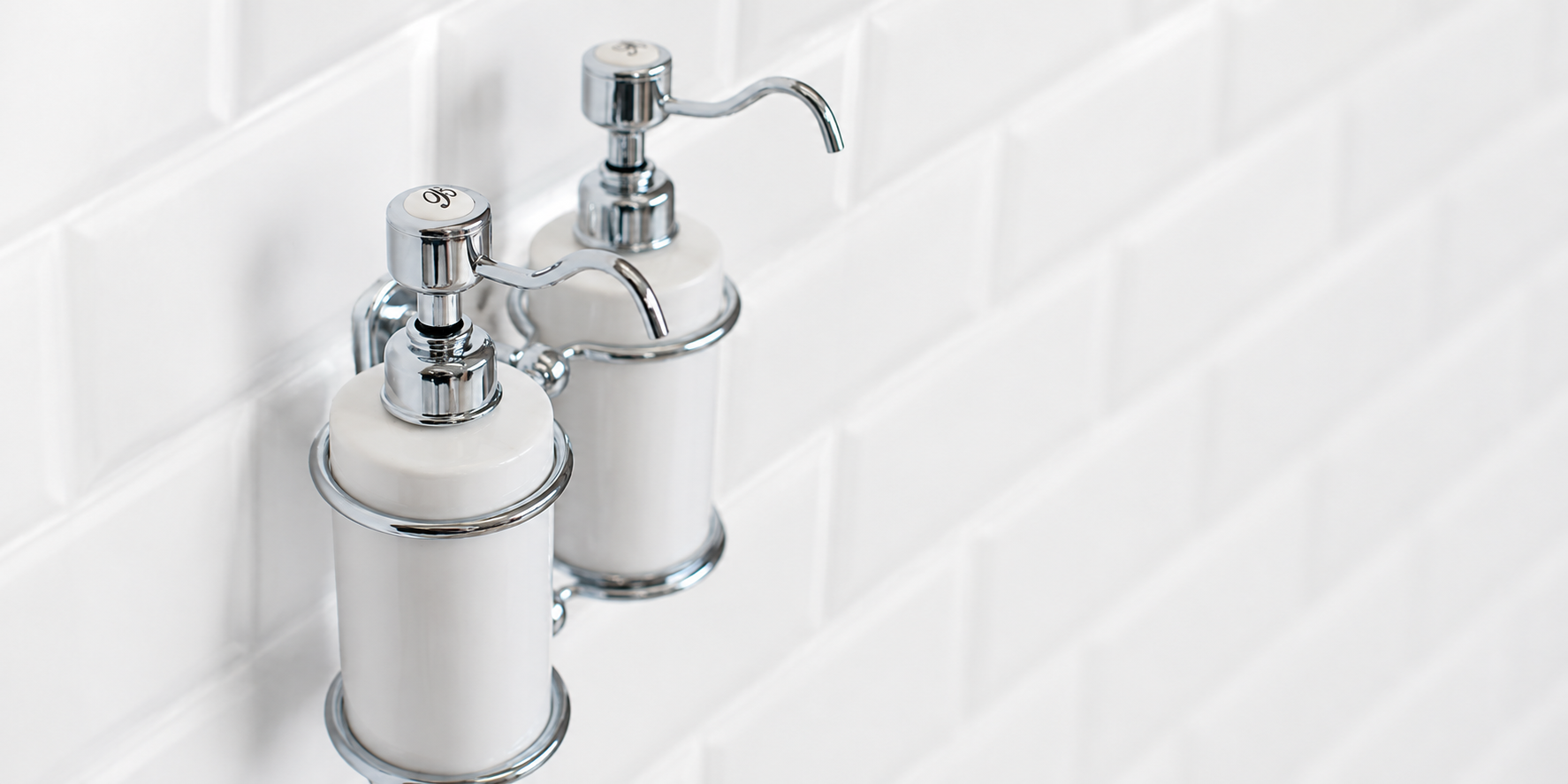 A pair of Burlington Soap Dispensers mounted on a white tiled bathroom wall