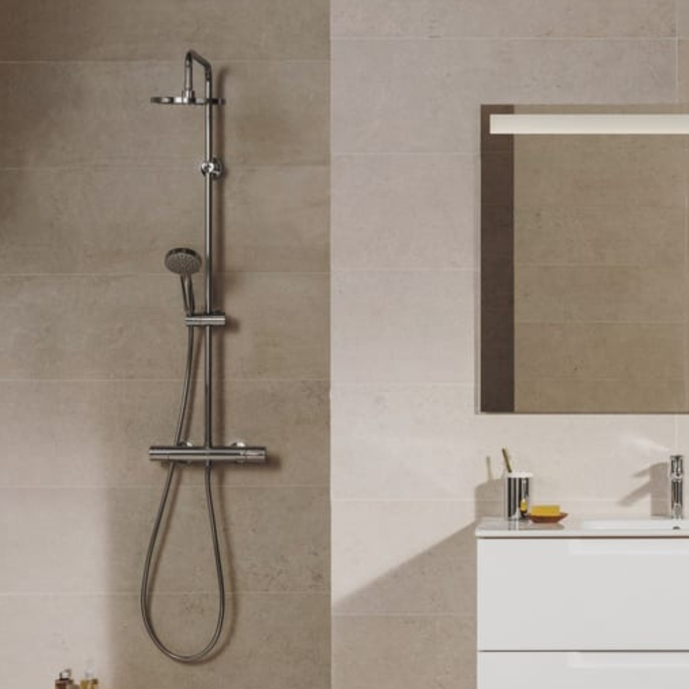 Lifestyle image of the Roca Victoria-T Chrome Thermostatic Shower Column mounted on a bathroom wall next to mirror and vanity unit basin