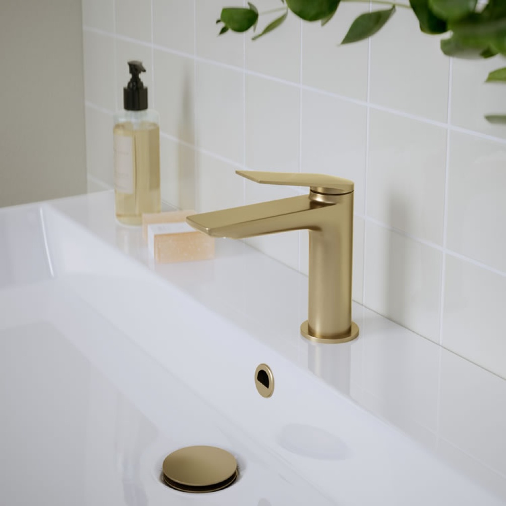 Photo of the Greenwich Basin Mixer in Brushed Brass with white tiles, leafy plant and hand soap