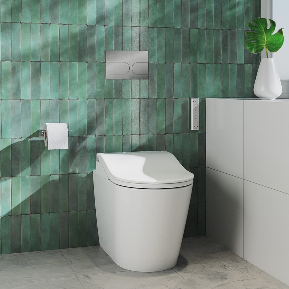 Lifestyle image of the TOTO Washlet RW Rimless Back to Wall Toilet installed in a bathroom with green tiled walls, next to a flush plate & toilet roll holder