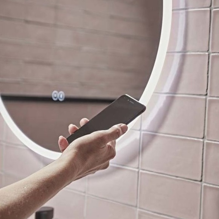 Product Lifestyle image of a man using his smart phone to control his Tavistock Resonate 600mm Circular Bluetooth Mirror