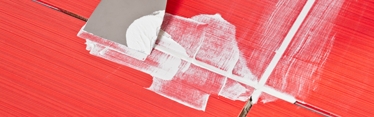 Close up image of someone applying grout to bathroom tiles with a trowel