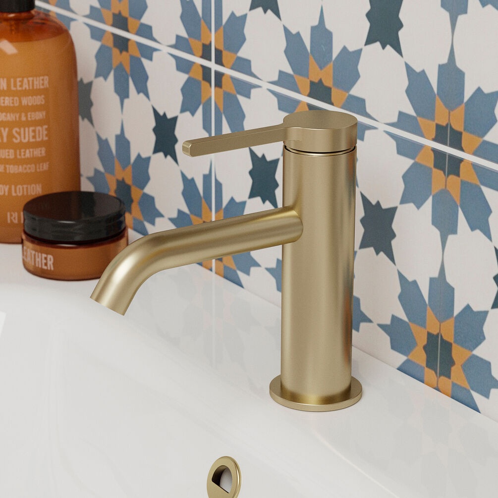 Product lifestyle image of Britton Hoxton 2.0 Slim Brushed Brass Mono Basin Mixer next to floral tile pattern on basin HOX110DNF