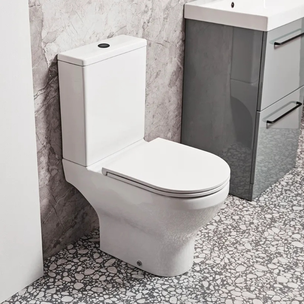 Lifestyle image of the Tavistock Micra Evo Close Coupled Open Back Toilet installed next to grey vanity unit & basin