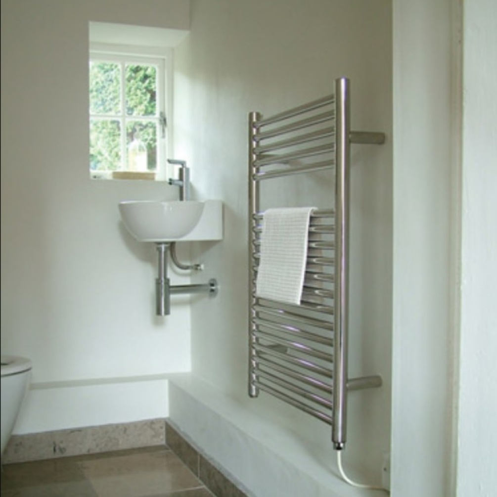 Product lifestyle image of The Sussex Range by JIS Coombe High Output Heated Towel Rail with white towel in light coloured bathroom space with cloakroom wall mounted basin COOMBE-P