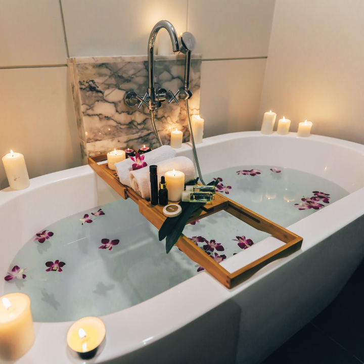 image of a bathtub filled with petal and multiple candles lit around with bath board filled with products