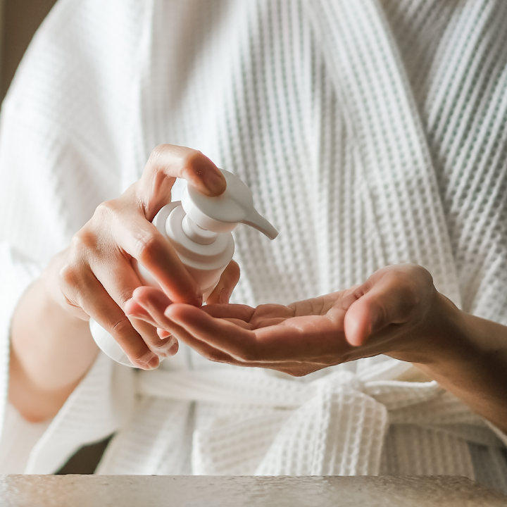 photo of person applying lotion to hand from pump bottle for skincare routine