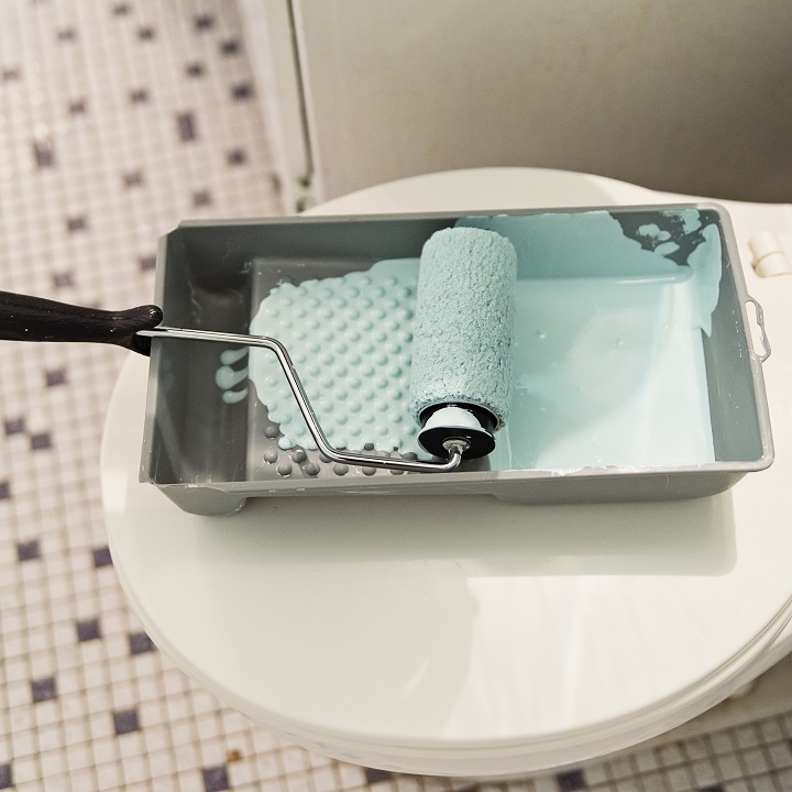 image of a closed toilet in a mosaic tiled bathroom with paint try and paint covered roller on top