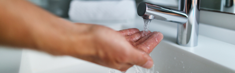 Close up image of a man's hand checking the water pressure from a mixer tap