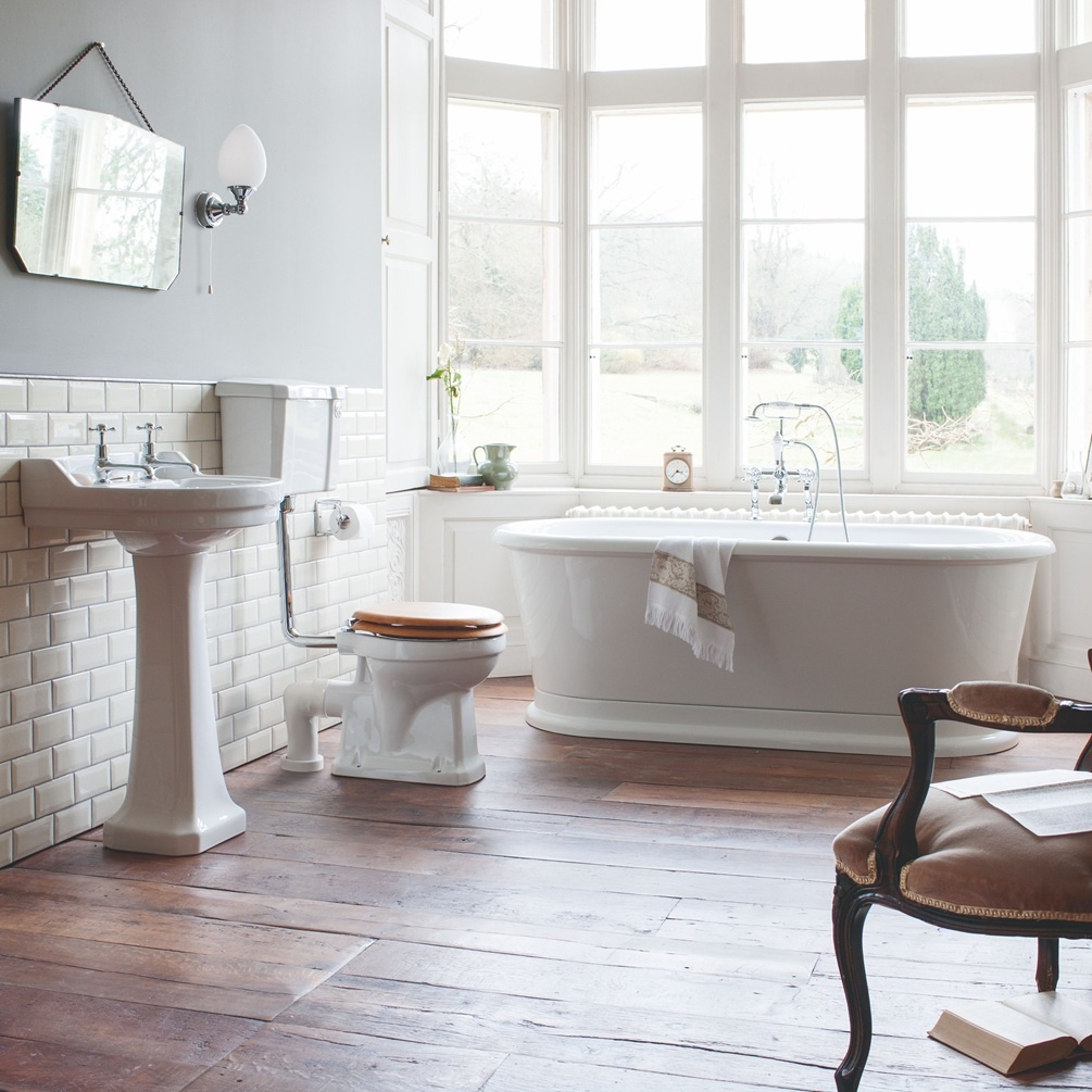 image of a burlington london freestanding bath, low level toilet and pedestal basin on a dark wood panel flooring in a room with big windows