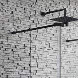 Product lifestyle image of Kudos Ultimate Matt Black Standard Front Panel Fixing Kit holding up screen fixed to grey brick wall 10WPFPFKMBK