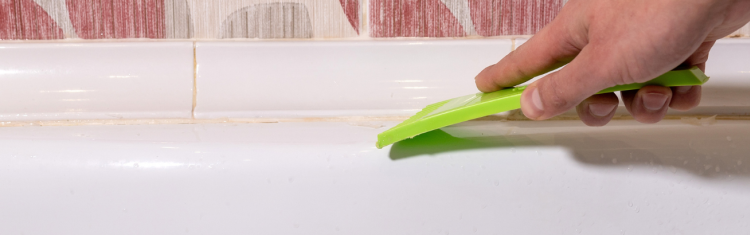 Close up image of a man removing old sealant with a scraping tool