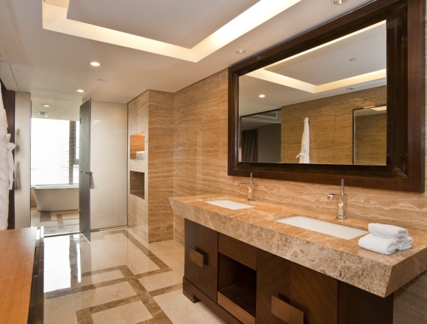 Lifestyle image of a Hotel style bathroom, with marble floor tiles, dark brown wooden cabinet and marble countertop, inset basins with chrome taps and a wooden backed rectangular mirror